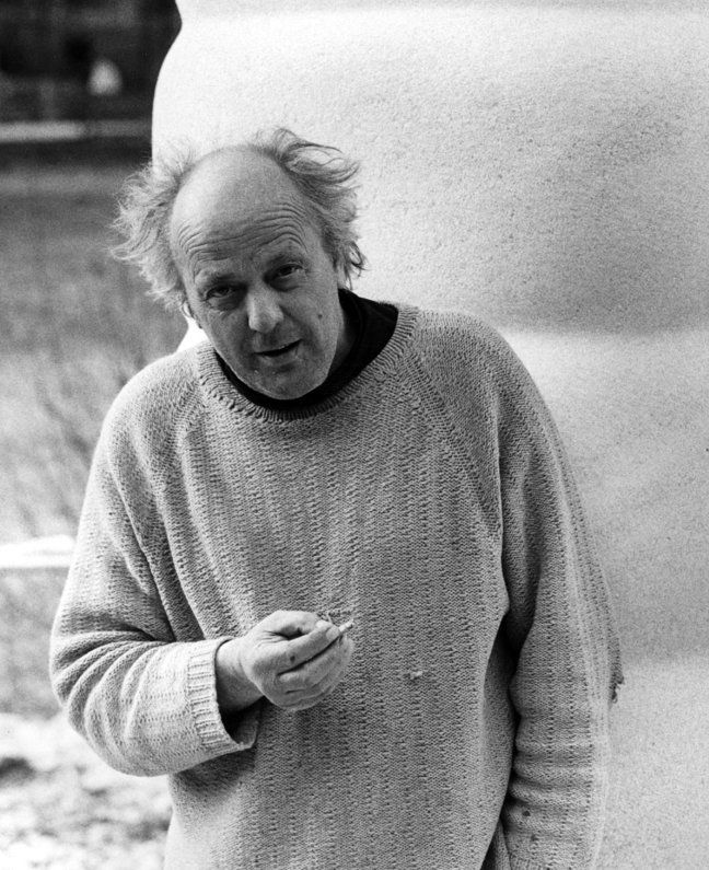 Der künstlre Otto Eder auf einem schwarz-weiß Bild. Er hällt seine zigarette und steht vor einer Skulptur. 